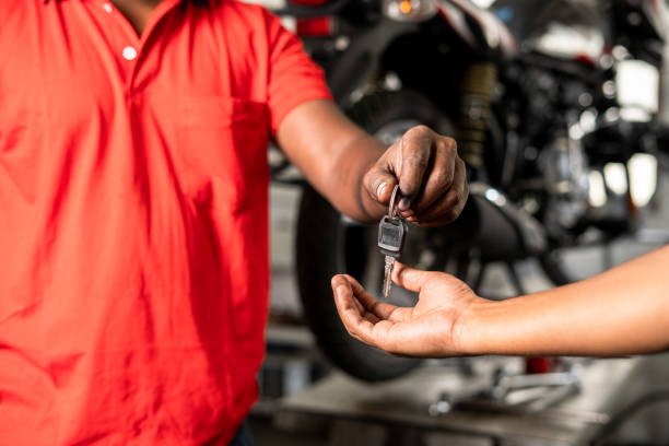 Close up of bike mechanic hands giving motorbike key to customer after maintenance service at garage - concept of successful completion repair service