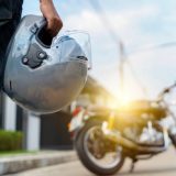 Grab your helmet and hit the road. a young man riding a motorbike through the city. Rear view of a biker in a leather jacket with a chopper holding a helmet