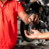Close up of bike mechanic hands giving motorbike key to customer after maintenance service at garage - concept of successful completion repair service.